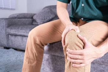 摄图网_325432851_青年男子坐在沙发上时膝盖疼痛 在家中享受保健医疗或日常生活概念的护理肌腱赛跑者药品运动事故成人男性身体肌肉扭伤（企业商用）