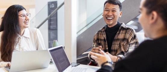 Students sitting at table with laptops laughing