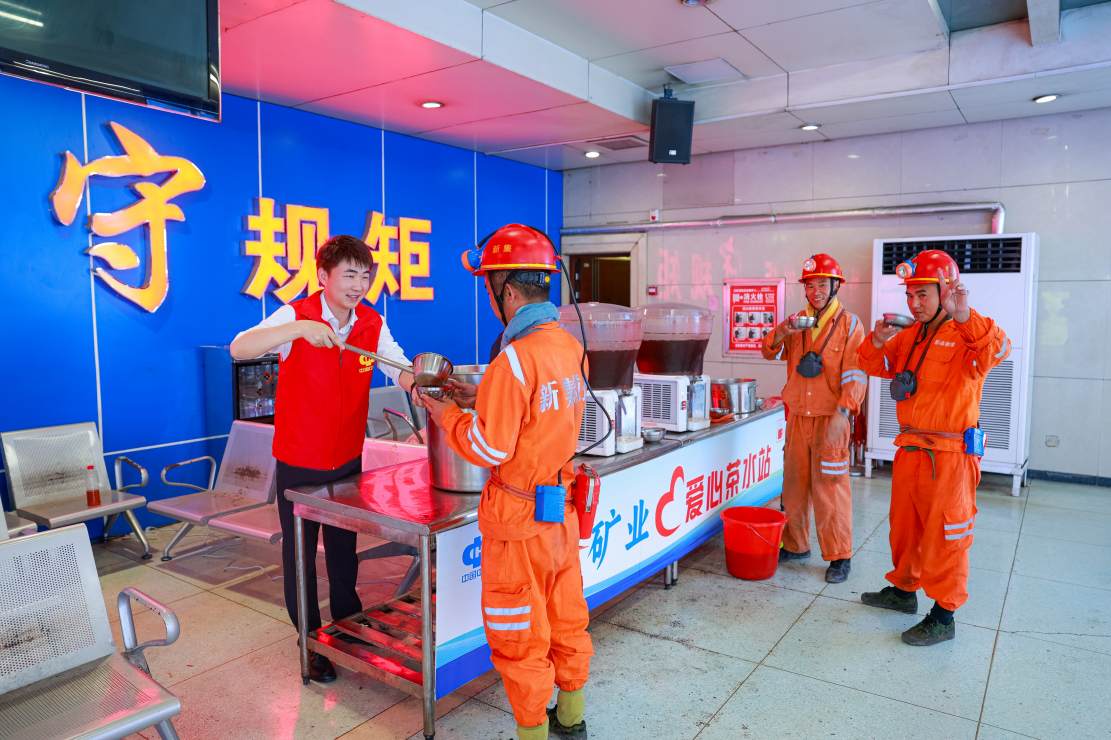 在刘庄矿业井口大厅爱心茶水站前 青年志愿者正细心为矿工舀取消暑饮品（陆刚）
